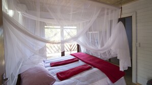 Een kamer met een bed, overdekt met een witte hemel, een raam met uitzicht, en een deur aan de rechterkant.