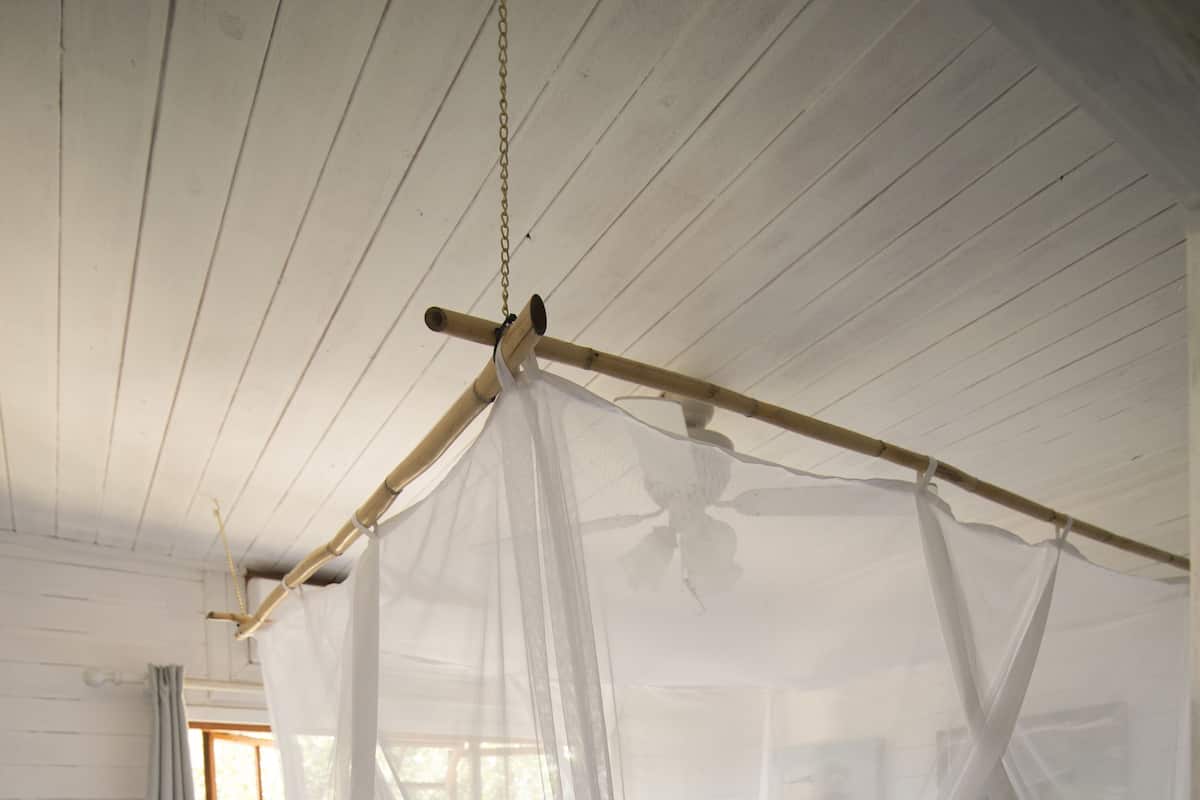 Een eenpersoonsbed met hemelbed, witte gordijnen en een houten vloer.