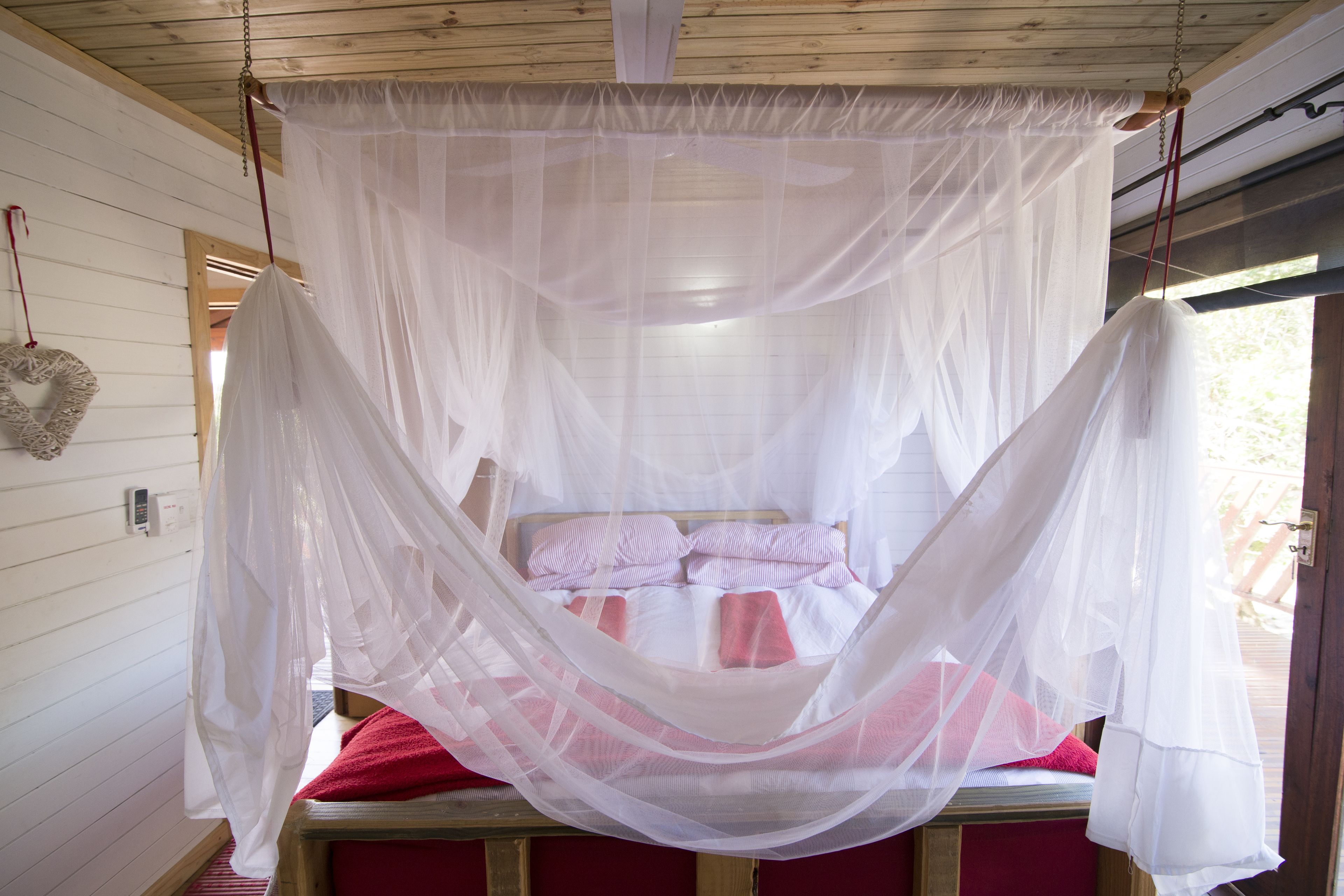A bed with a white canopy and red bedding in a room with wooden walls and a window.