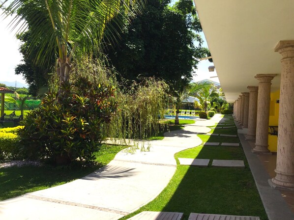 Un chemin bordé de palmiers et de verdure, menant à un bâtiment doté de colonnes.