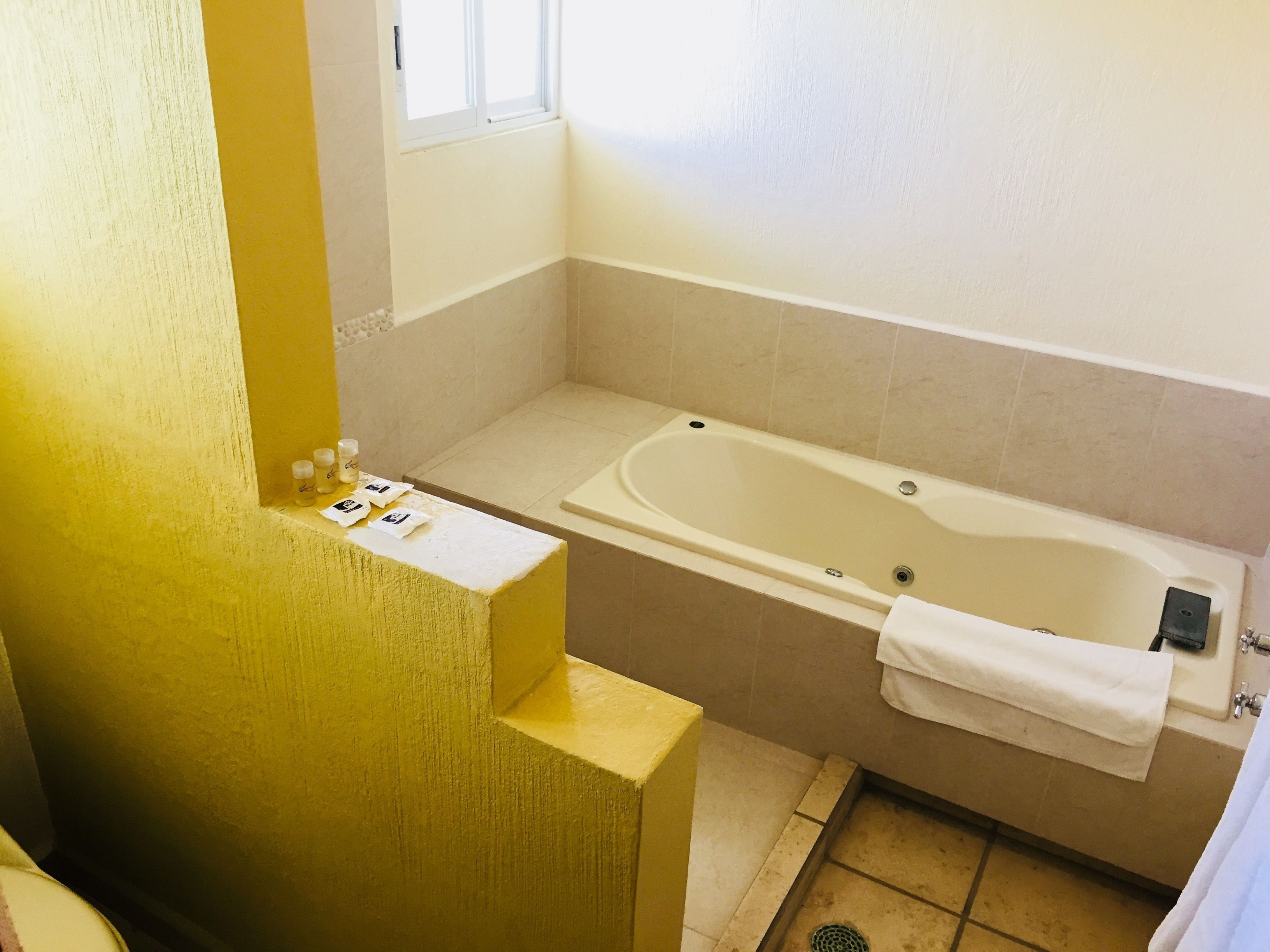 Ein Badezimmer mit Badewanne, Fenster und gelber Wand.