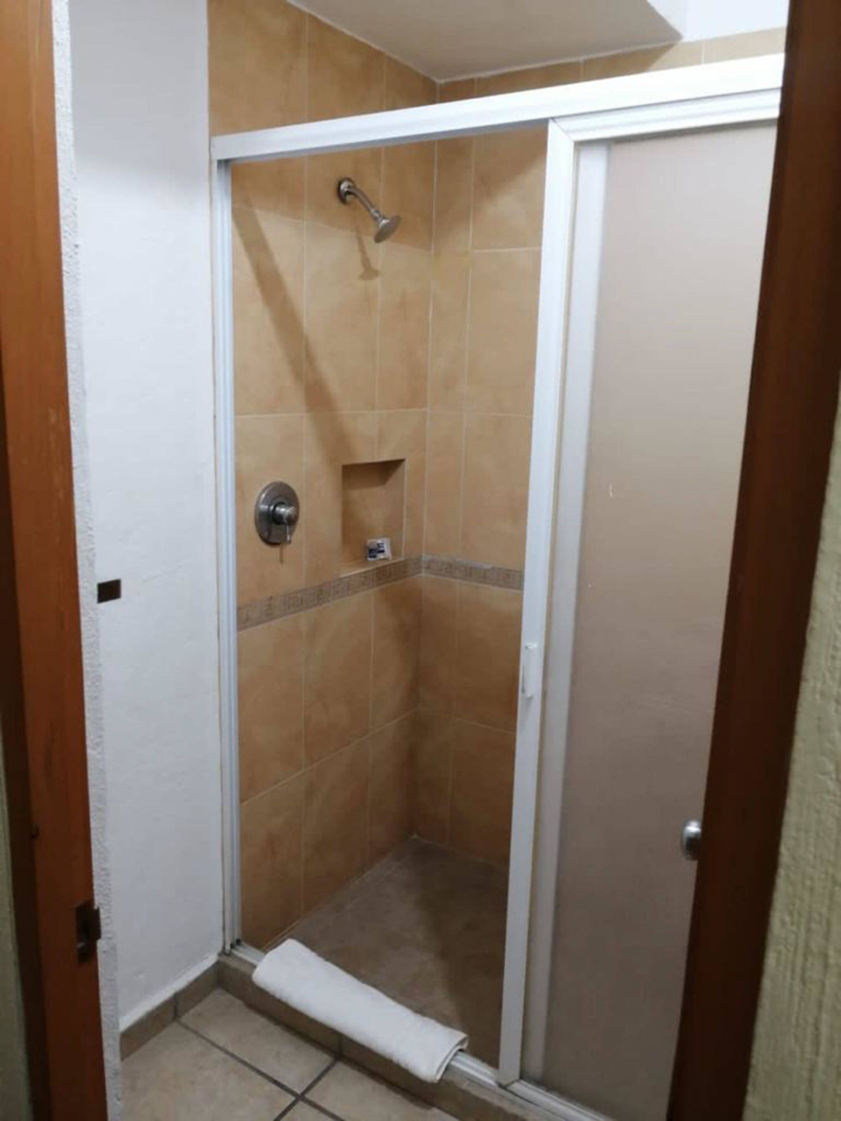 A small, enclosed shower area with beige tiles, a showerhead, and a towel on the floor.