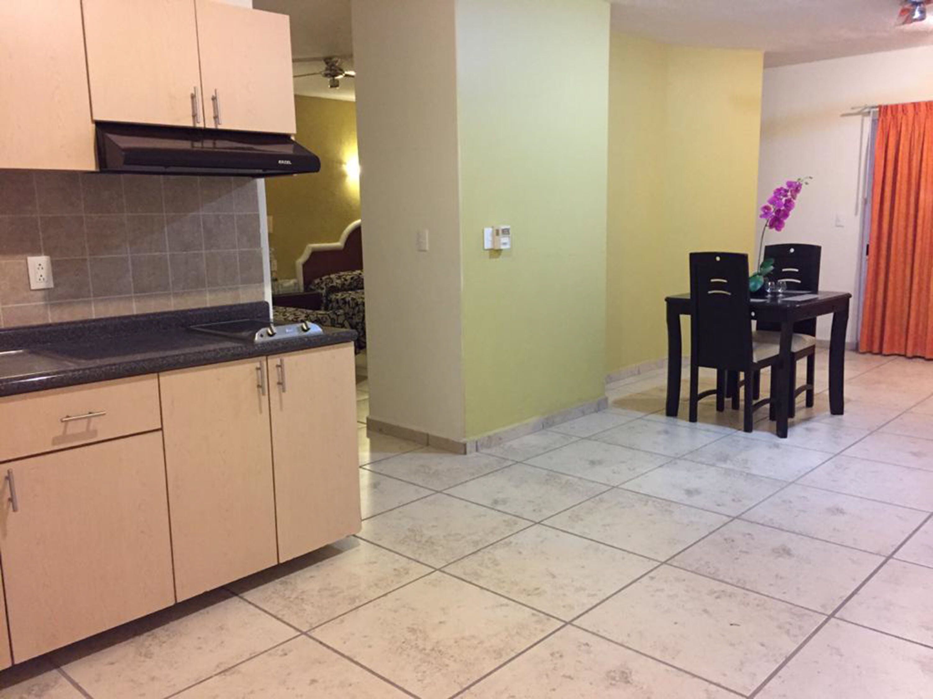 A kitchen with beige cabinets, a black countertop, and a tiled floor. There is a dining area with a table and chairs.