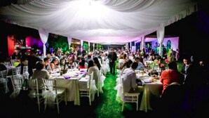 A banquet hall with white tables and chairs, a green carpet, and a stage with colorful lighting. - Hotel JS (Yautepec)