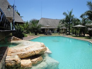 Piscina con una formación rocosa, sillas de descanso y palmeras.