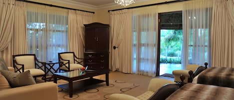 A spacious living room with a large wooden cabinet, two armchairs, a sofa, and a coffee table.