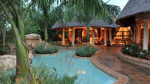 Une piscine entourée de plantes tropicales et bordée d’une structure à toit de chaume.