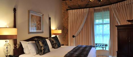 Quarto de hotel bem equipado, com uma cama grande, uma escrivaninha com luminária, uma cadeira e um guarda-roupa.