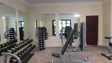 Een fitnessruimte met diverse trainingsapparaten, waaronder gewichten, een bankdrukapparaat en een hometrainer.