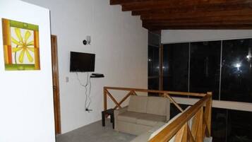 Una habitación con escalera de madera, televisor de pantalla plana en la pared y ventana con vista al cielo nocturno.