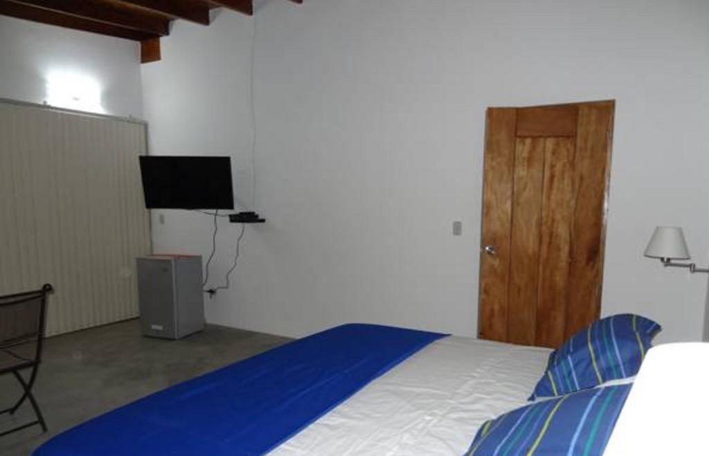 Une chambre à coucher avec un lit, une porte en bois, un téléviseur fixé au mur et un bureau avec un ordinateur.
