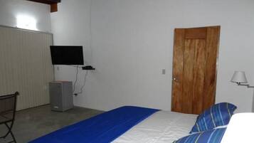 Une chambre à coucher avec un lit, une porte en bois, un téléviseur fixé au mur et un bureau avec un ordinateur.