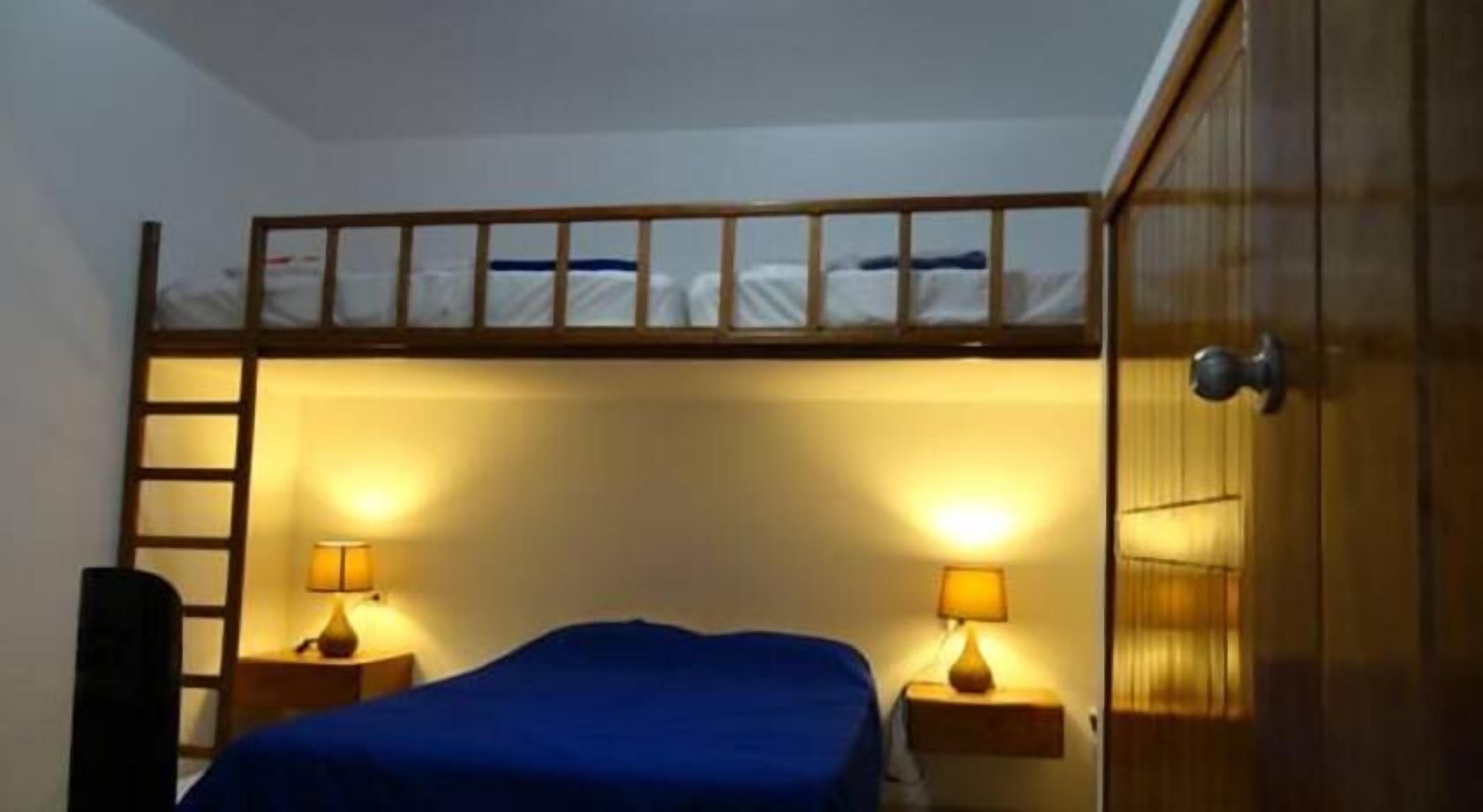 Dormitorio con literas, una escalera, dos lámparas de noche y un armario.