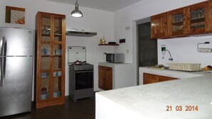 A modern kitchen with a stainless steel refrigerator, a built-in oven, a microwave, wooden cabinets, and a white countertop. - Casa de Playa Akas (Canoas de Punta Sal)