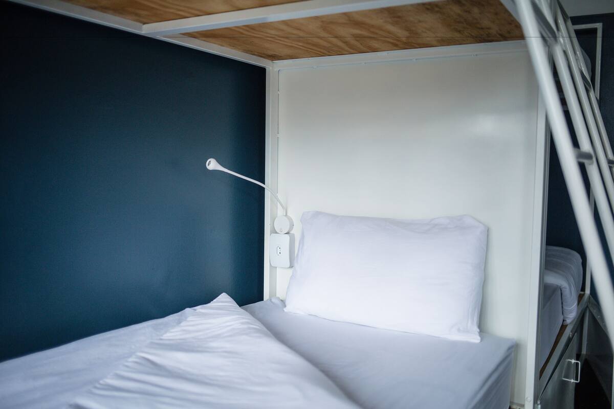 Una cama individual con ropa de cama blanca en una habitación con paredes azul oscuro y techo de madera.