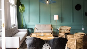A room with a teal wall, a white sofa, a wooden coffee table, wicker chairs, and a large plant.