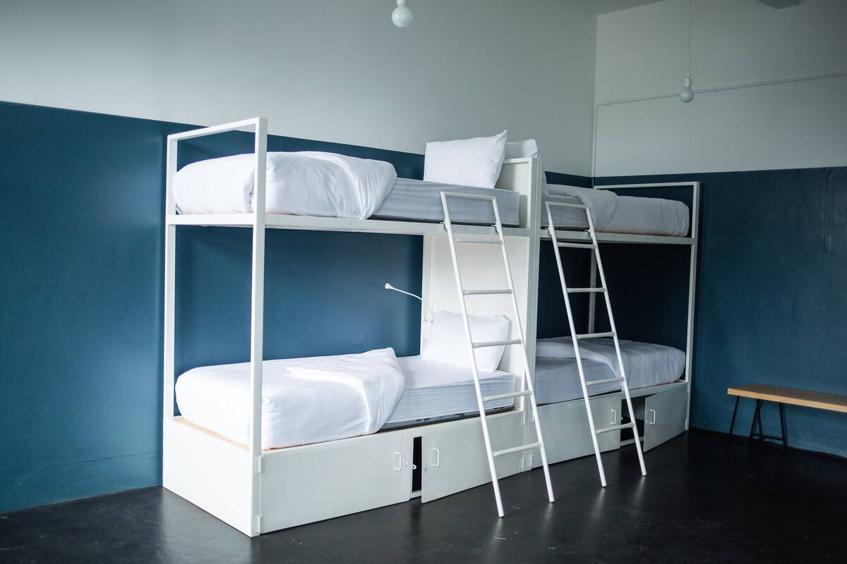 Una cama litera con escalera, un escritorio pequeño y una lámpara.