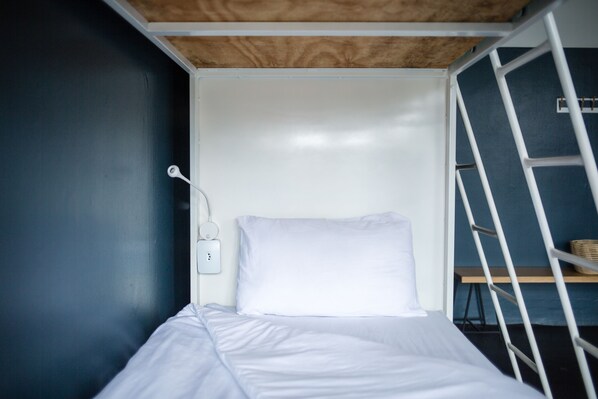 A small, single-bed room with a white mattress and pillow, a white wall, and a wooden ceiling. - Curiocity Durban - Hostel (Durban)