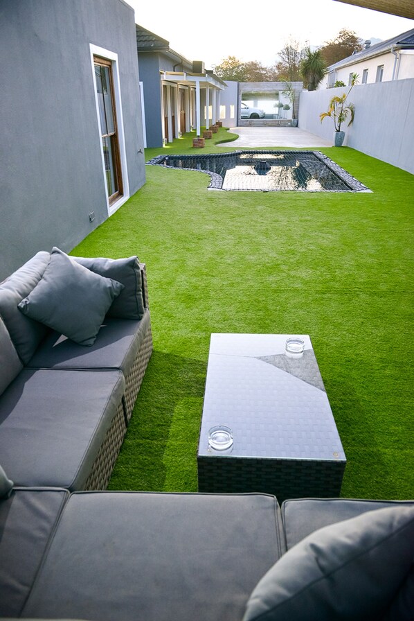 A modern outdoor patio with a grey sofa, a small table, and a well-maintained lawn.
