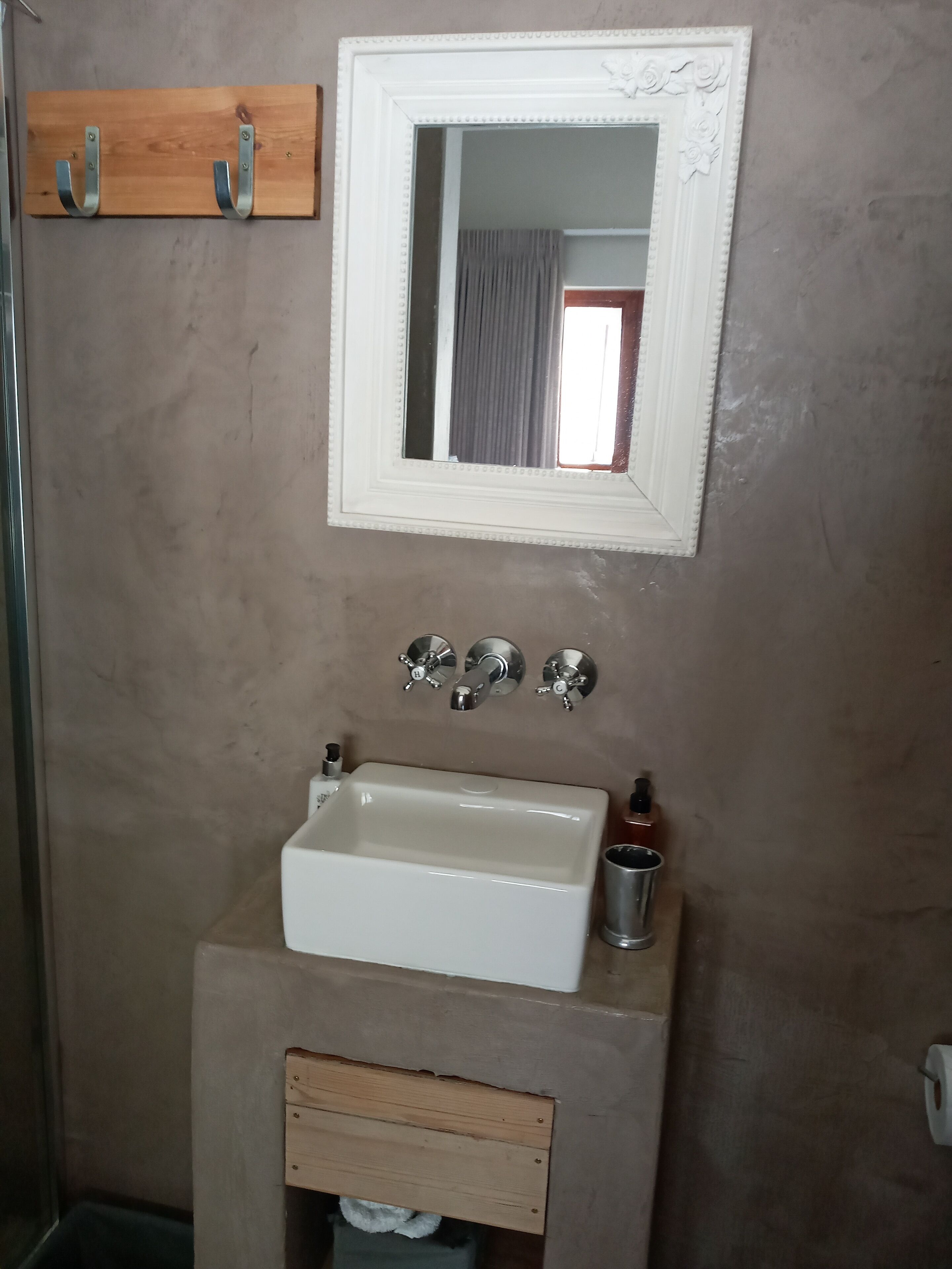 A bathroom with a white sink, a mirror, and a wooden shelf above it.