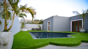 A modern outdoor pool area with a stone deck, a small seating area, and a well-maintained lawn.