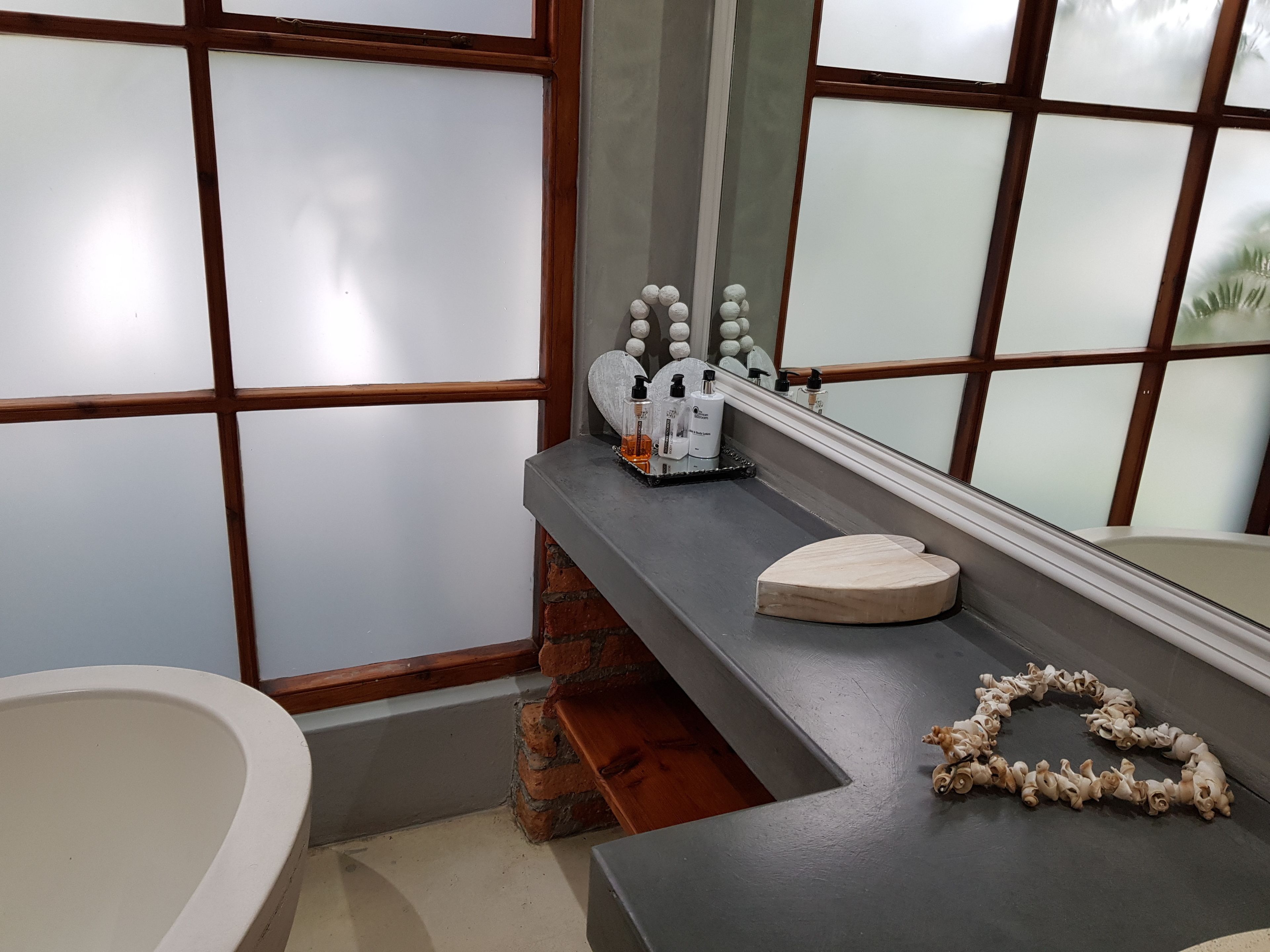 A bathroom with a large window, a bathtub, a vanity with toiletries, and a mirror.