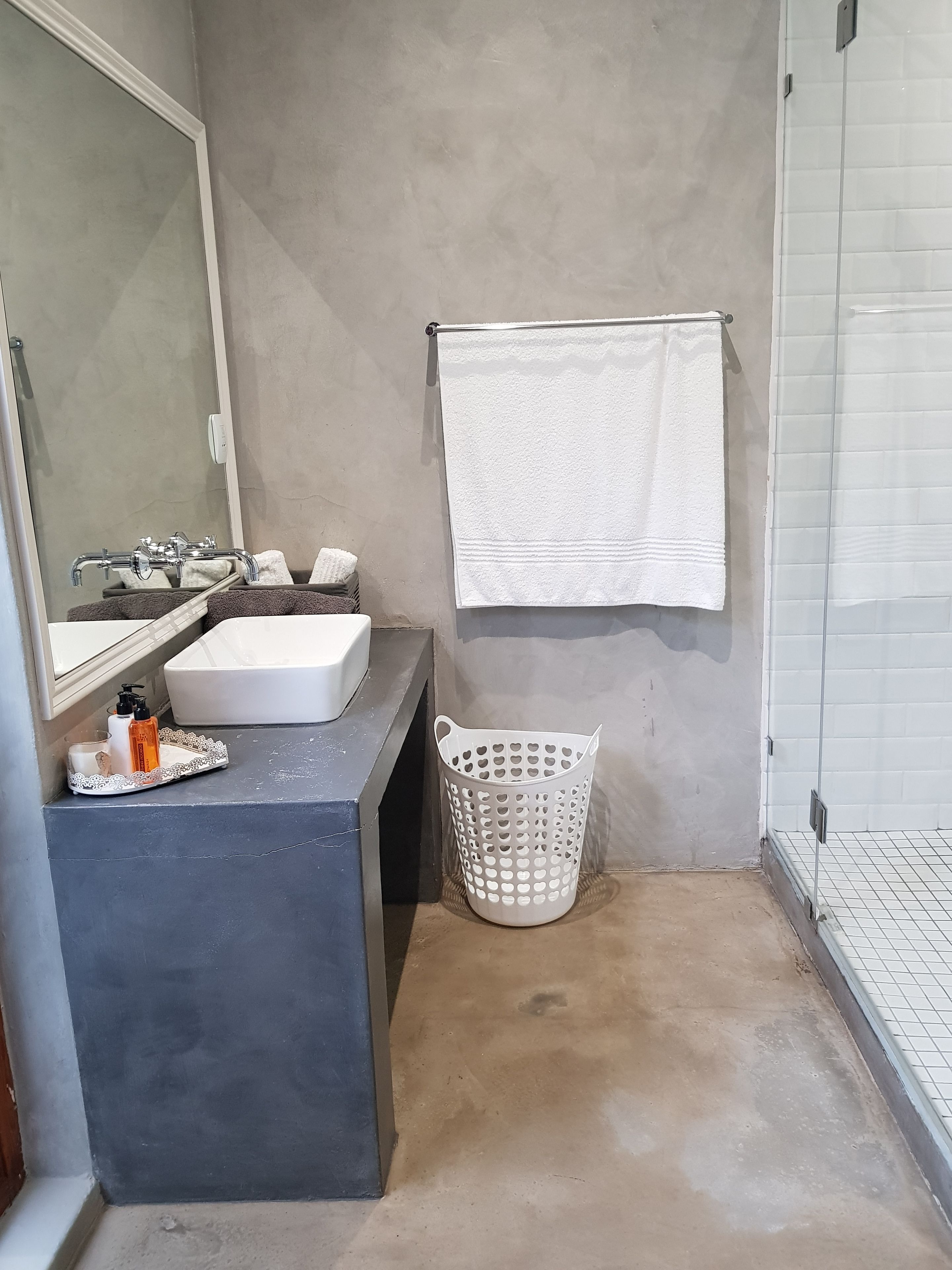 A bathroom with a white sink, a mirror, a towel hanging on the wall, and a white laundry basket.
