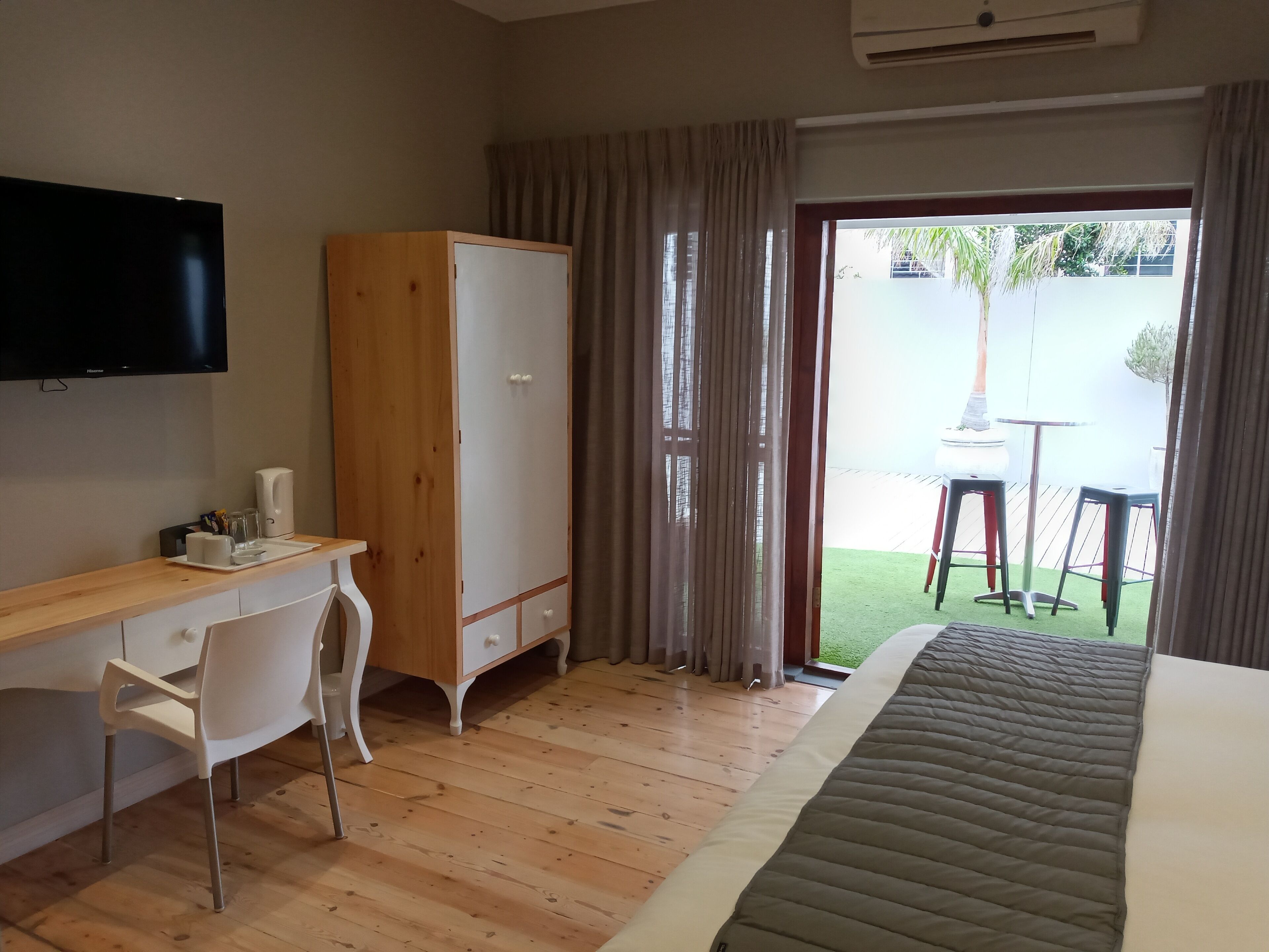 Habitación de hotel con un escritorio de madera, una silla blanca, un armario, una cama y un televisor.