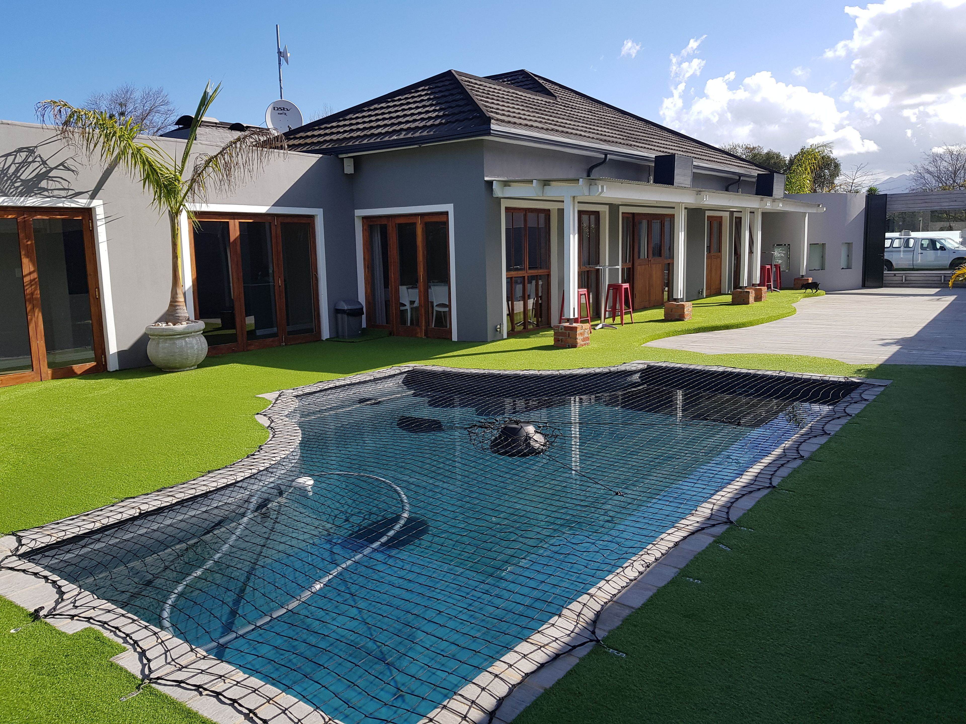 A modern house with a swimming pool, a covered patio, and a well-maintained lawn.