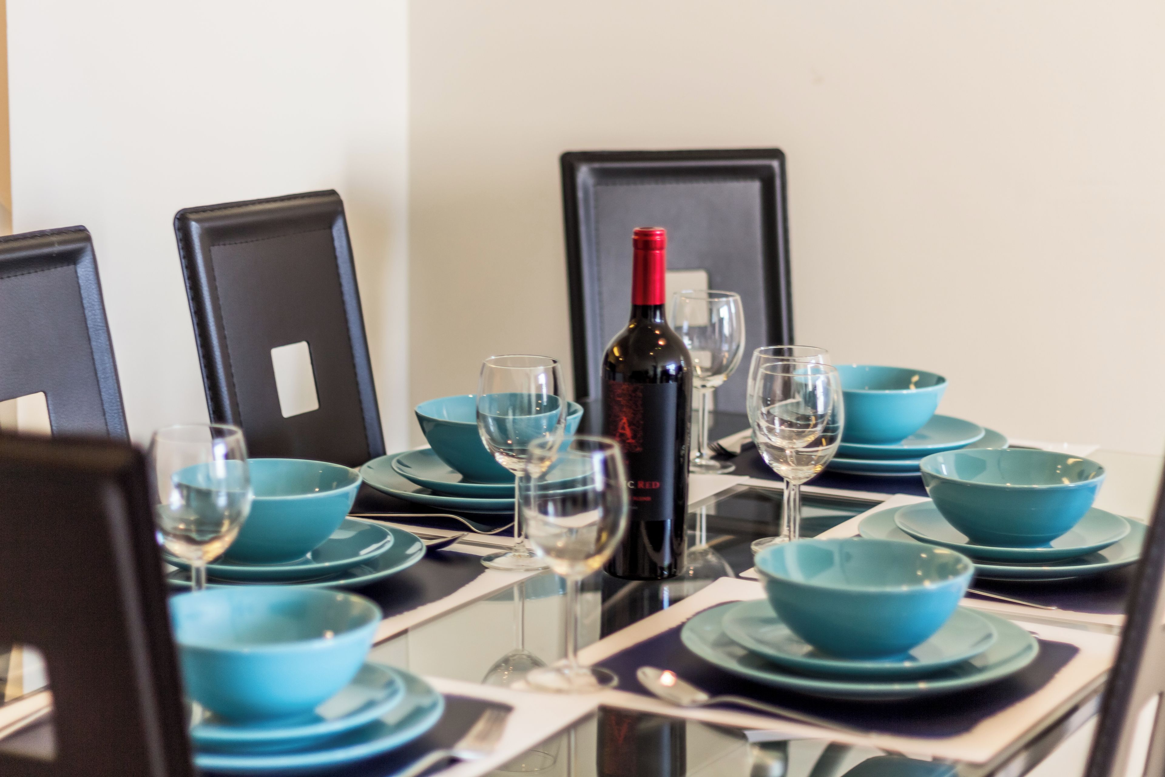 A dining table set with blue bowls, wine glasses, and a bottle of red wine.