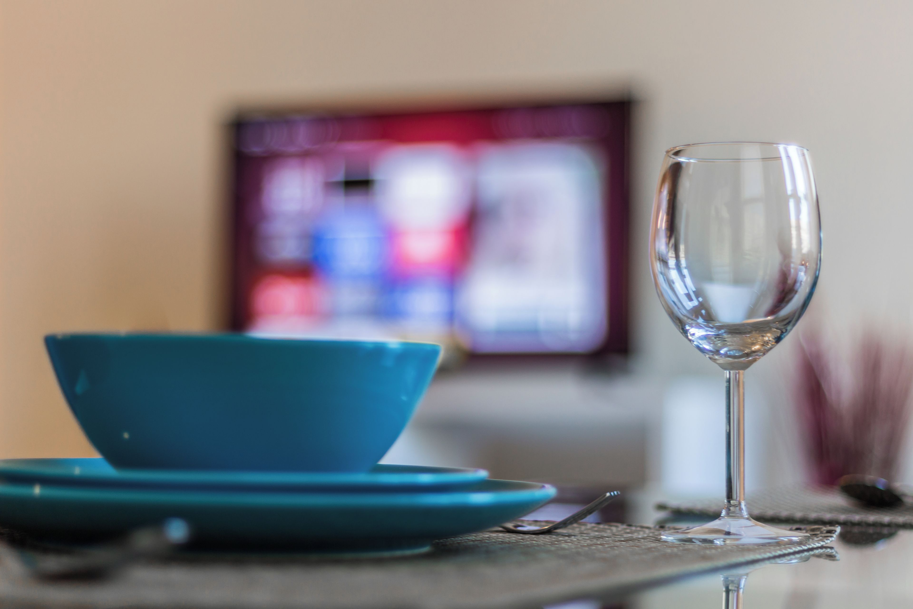 A dining table with a clear glass wine glass, a blue bowl, and a plate.