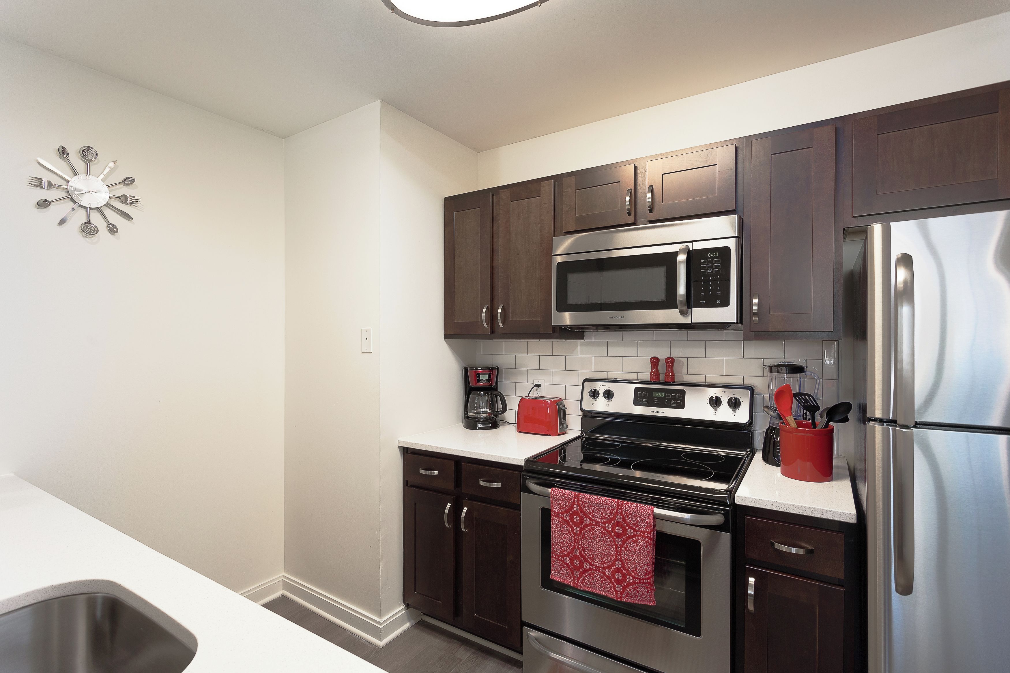 A modern kitchen with stainless steel appliances, dark wooden cabinets, and a white countertop.