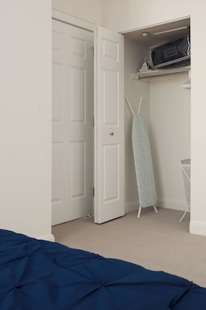 A bedroom with a bed, a door, an ironing board, and a shelf with a bag. - Fully Furnished Apartment in Philadelphia (Philadelphia)