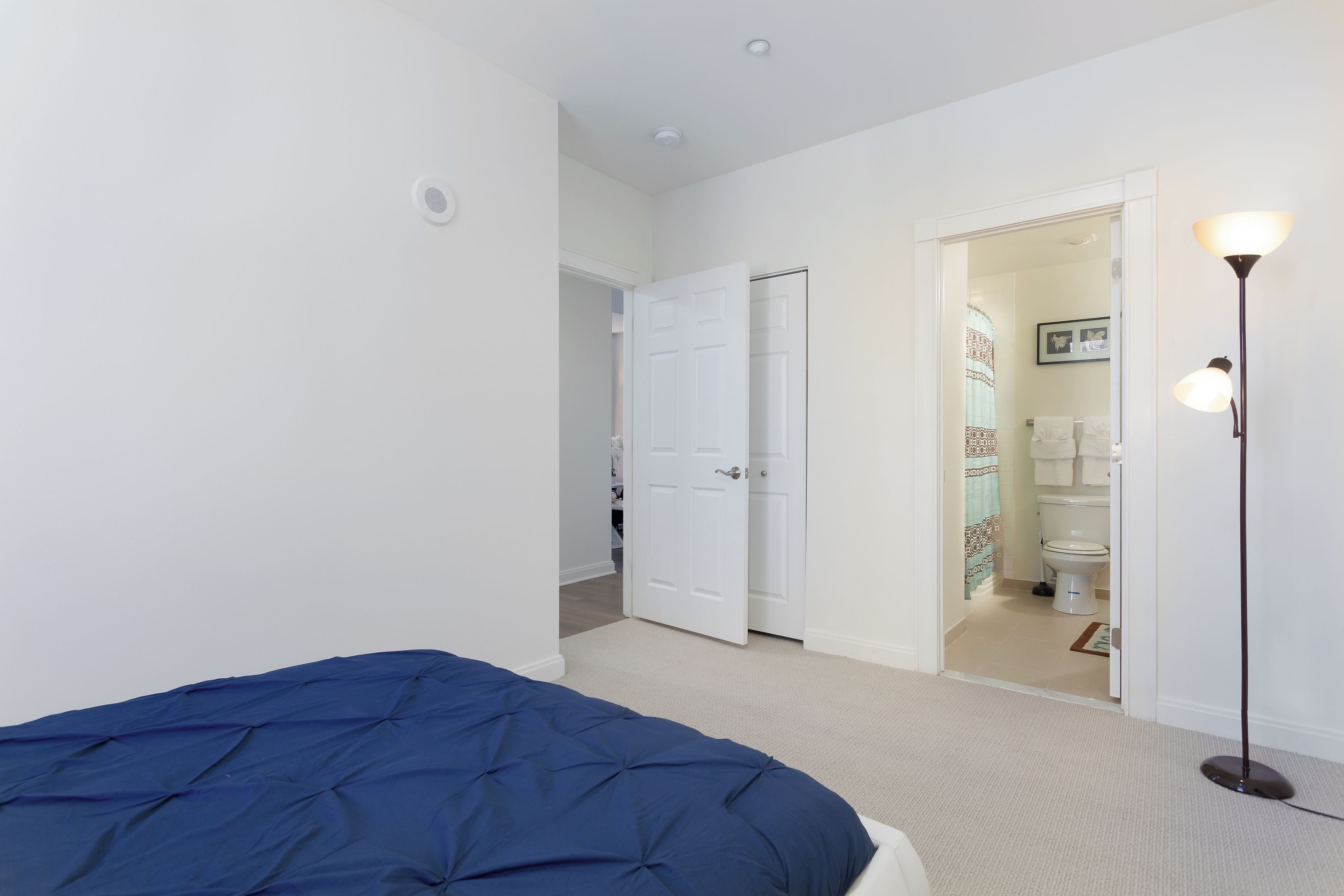 Une chambre à coucher avec un lit, une porte donnant sur une salle de bain et une lampe sur pied.
