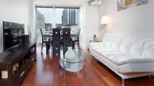 A modern living room with a white sofa, a glass coffee table, and a dining area with a glass table and chairs. - Pelican Fully Furnished Apartments (Philadelphia)