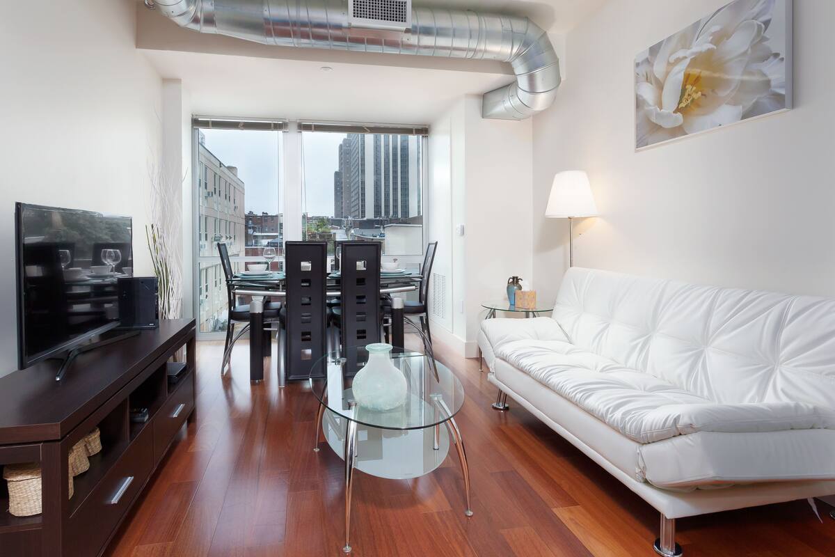 A modern living room with a white sofa, a glass coffee table, and a dining area with a glass table and chairs.