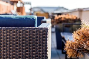 Wicker furniture with cushions, a plant, and a building in the background. - Pelican Fully Furnished Apartments (Philadelphia)