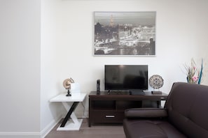 A living room with a flat-screen TV on a dark wooden stand, a globe on a white side table, and a framed cityscape photo above the TV. - Fully Furnished Apartment in Philadelphia (Philadelphia)
