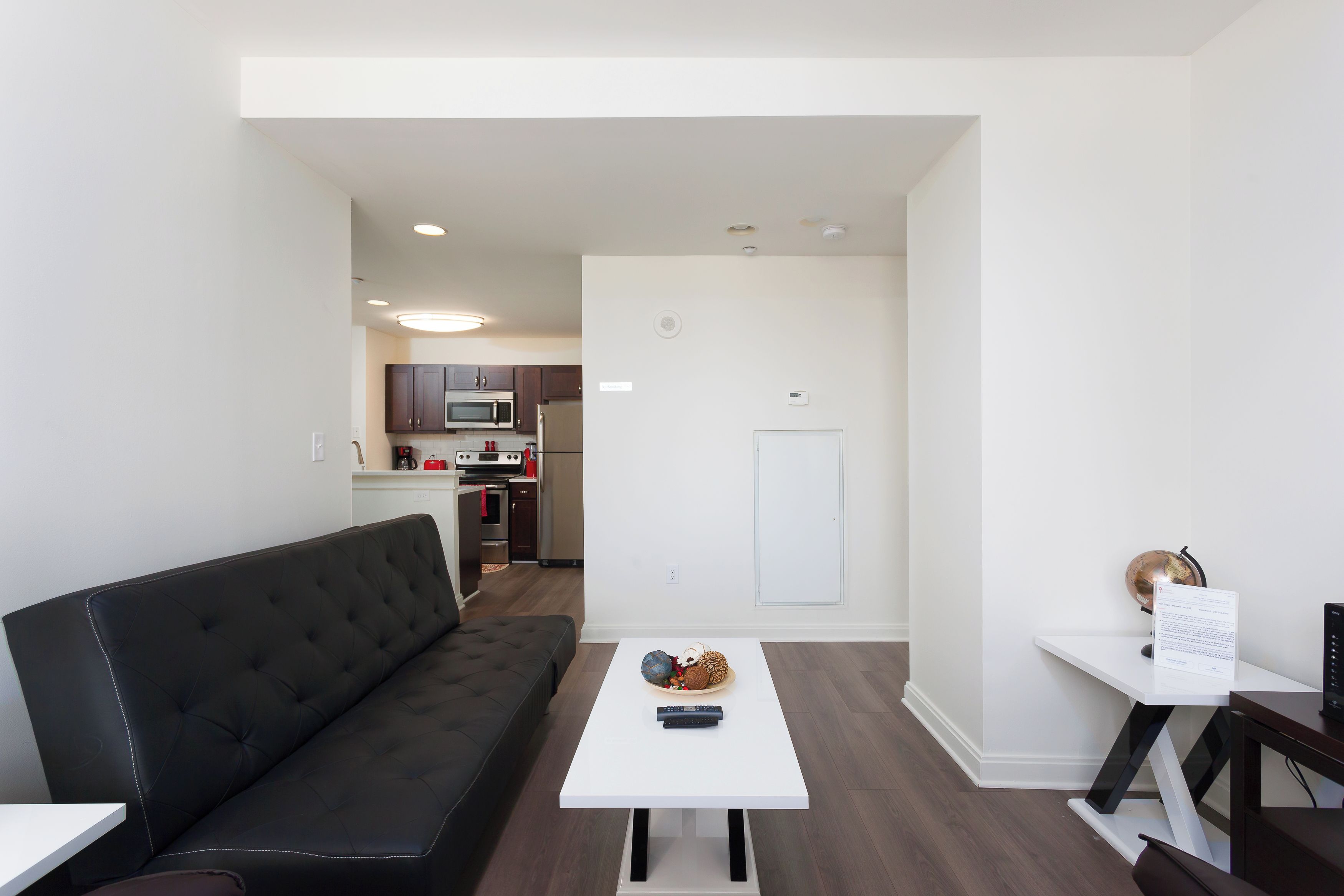 A modern living room with a black sofa, a white coffee table, and a kitchen in the background.
