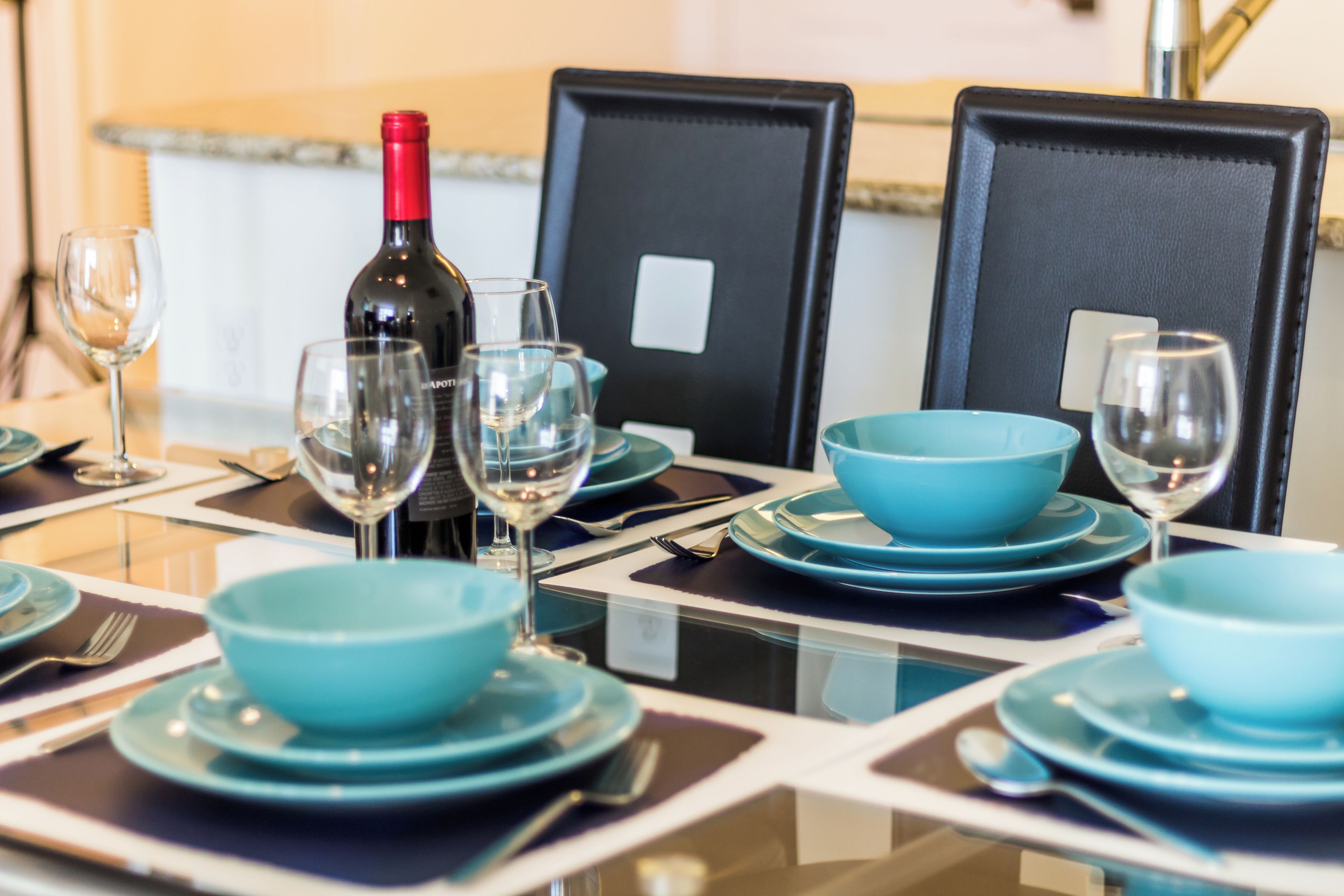 A dining table set with blue plates, bowls, and wine glasses, with a bottle of wine on the table.