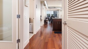 A modern interior with a wooden floor, a kitchen area with a window, and a door with a handle. - Pelican Fully Furnished Apartments (Philadelphia)