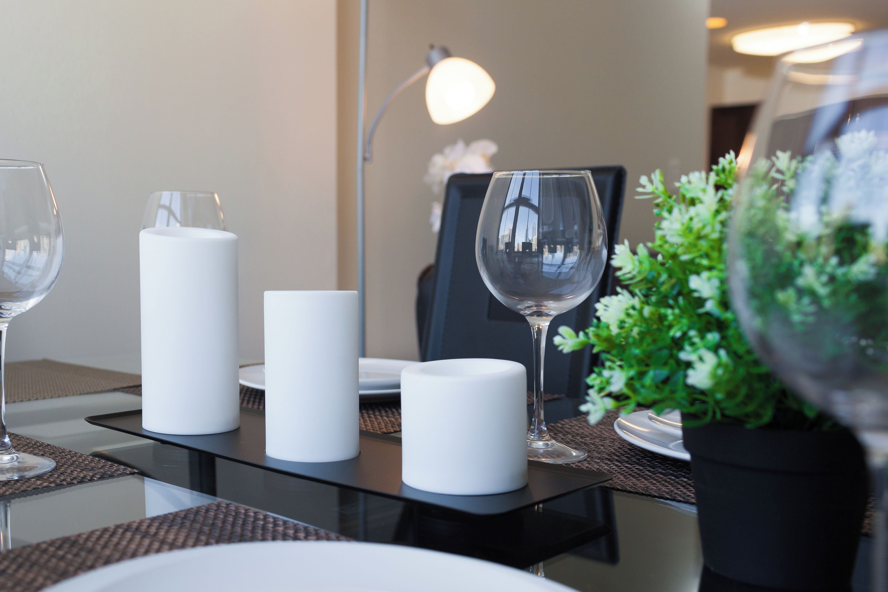 A dining table with candles, a glass, and a potted plant.