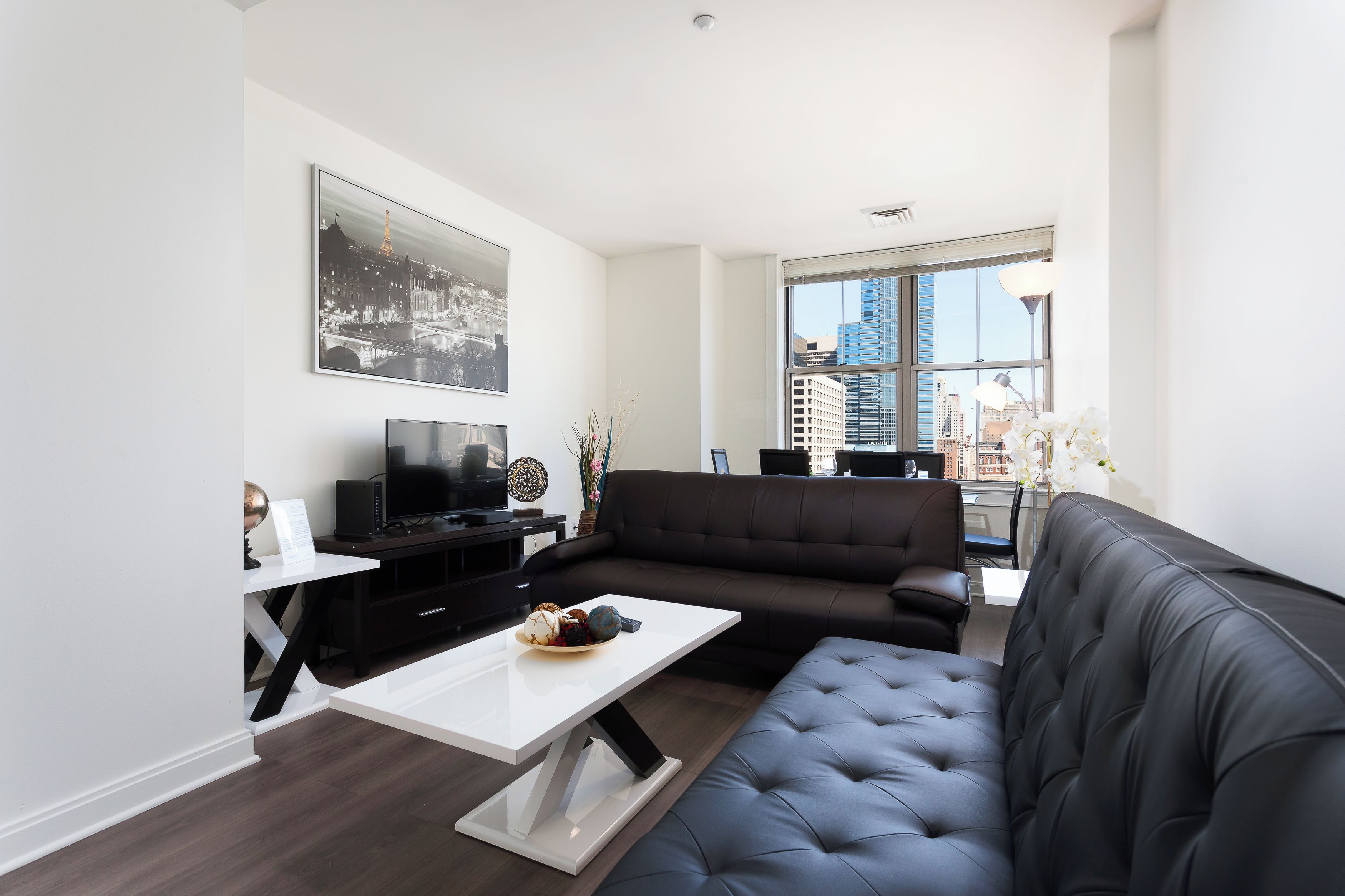 Een moderne woonkamer met een zwarte leren bank, een witte salontafel en een flatscreen televisie op een zwart meubel.