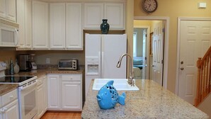 A kitchen with white cabinets, a granite countertop, a fish-shaped soap dish, a microwave, a toaster, and a refrigerator. - Turtle Bay 10 3 Bedroom Holiday Home By My Ocean Rentals (Folly Beach)