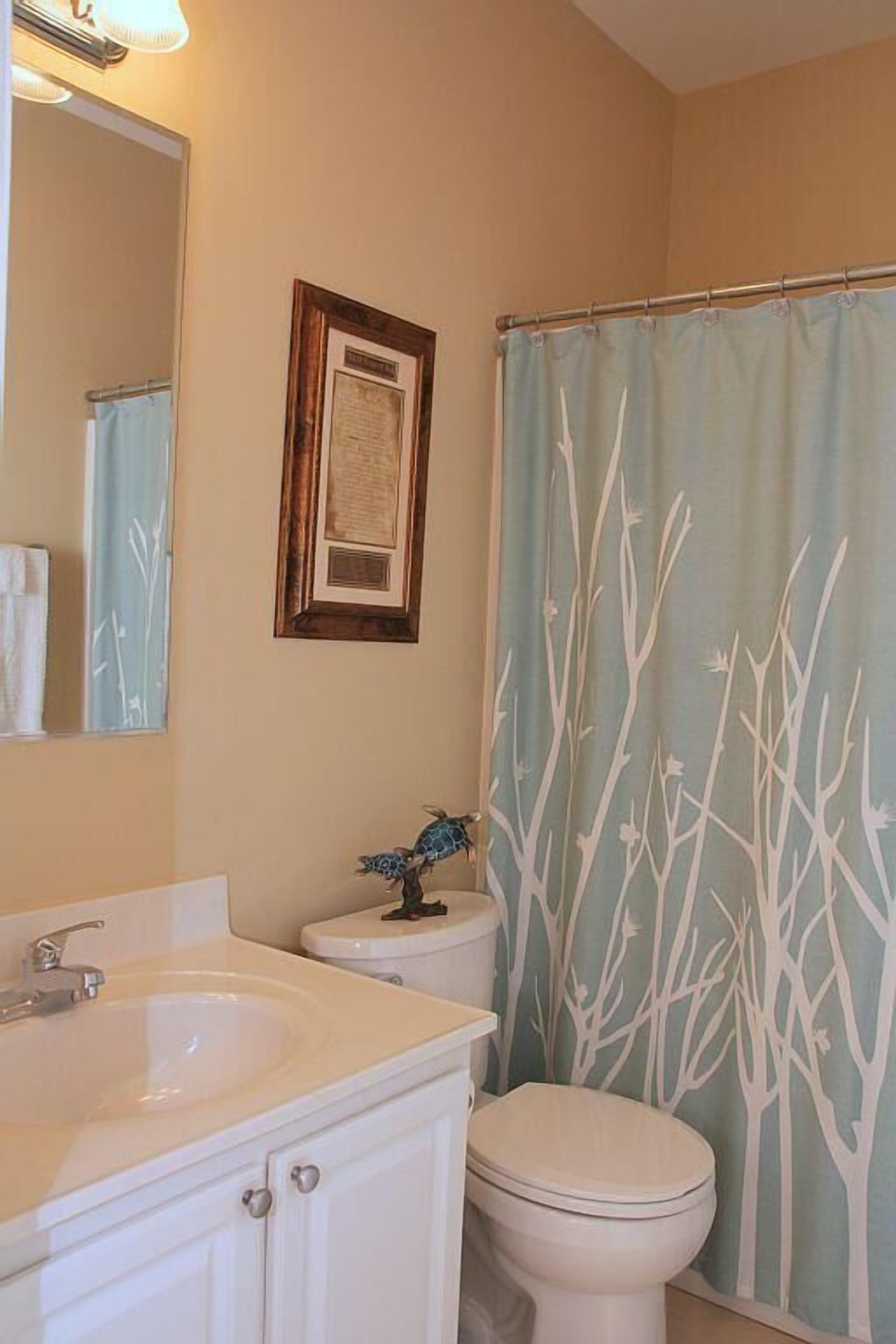 Un baño con lavamanos blanco, inodoro y cortina de ducha con estampado de árboles.