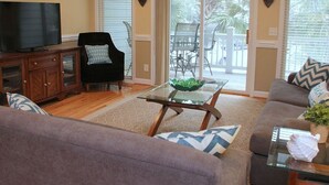 A living room with a television, a glass coffee table, a sofa, and a dining area with chairs and a table. - Turtle Bay 10 3 Bedroom Holiday Home By My Ocean Rentals (Folly Beach)