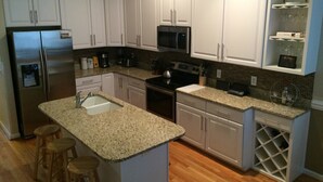A modern kitchen with white cabinets, stainless steel appliances, a granite countertop, and a wine rack. - Waters Edge 113 Community 3 Bedroom Holiday Home By My Ocean Rentals (Folly Beach)