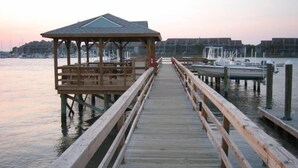 A wooden pier leading to a gazebo with a roof, extending over calm water with boats docked nearby. - Waters Edge 113 Community 3 Bedroom Holiday Home By My Ocean Rentals (Folly Beach)