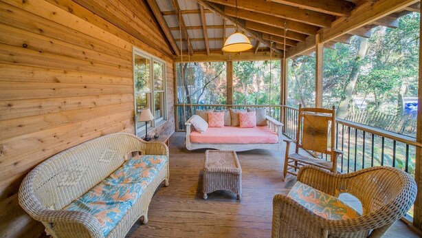 A wooden cabin with a porch, wicker furniture, and a pink sofa.