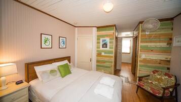 A hotel room with a wooden bed, a nightstand with a lamp, a chair with a floral pattern, and a wall with a striped design.